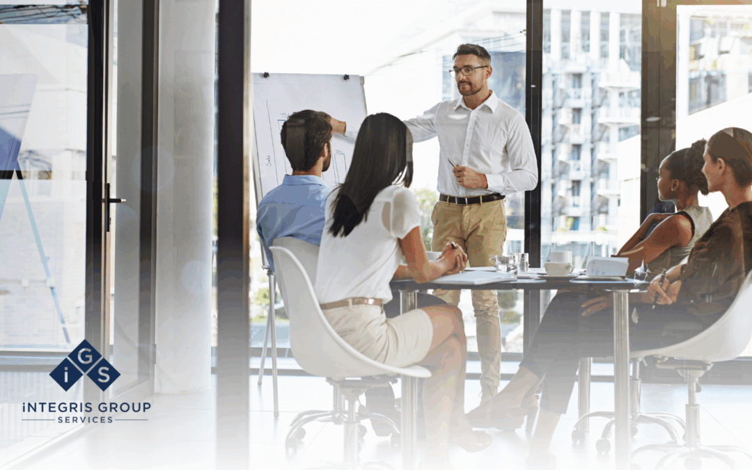 Business meeting with a presenter explaining strategies on a whiteboard to engaged participants, featuring Integris Group Services branding.